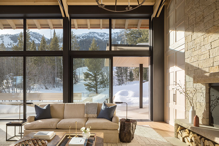 The great room features two fireplaces, and views of the Snake River Range. The paneling that flanks the limestone on this half of the room is actually a hidden doorway crafted and installed by Willow Creek Woodworks.